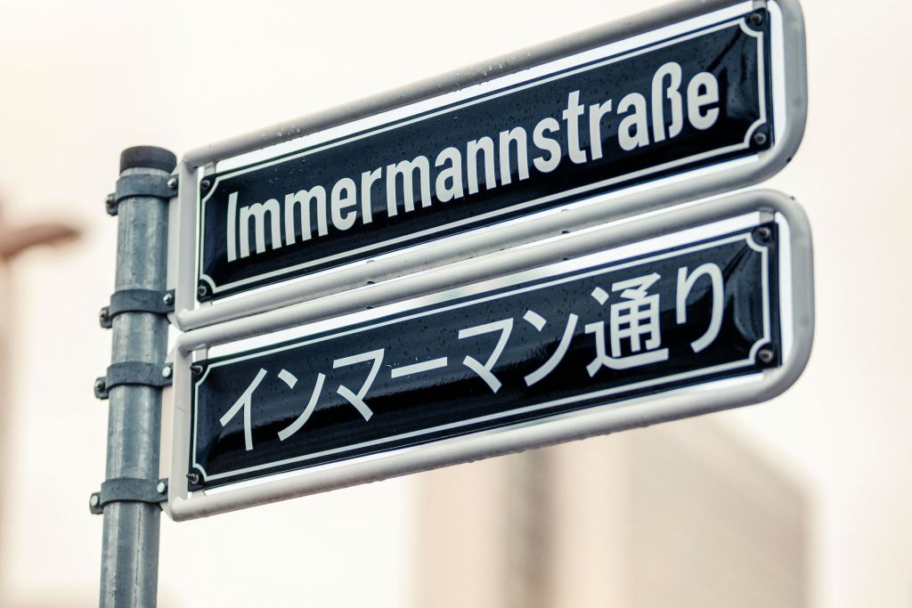 독일어와 일본어로 된 두 개의 거리 표지판, 둘 다 금속 기둥에 장착된 "Immermannstraße" 를 읽습니다.