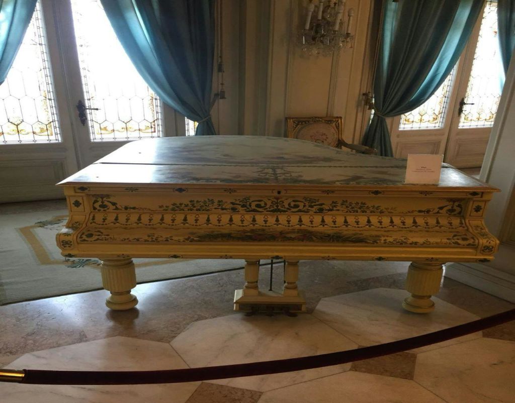 청록색 커튼, 샹들리에, 피아노 뚜껑에 팻말이 놓인 우아한 방에 있는 화려한 빈티지 피아노.