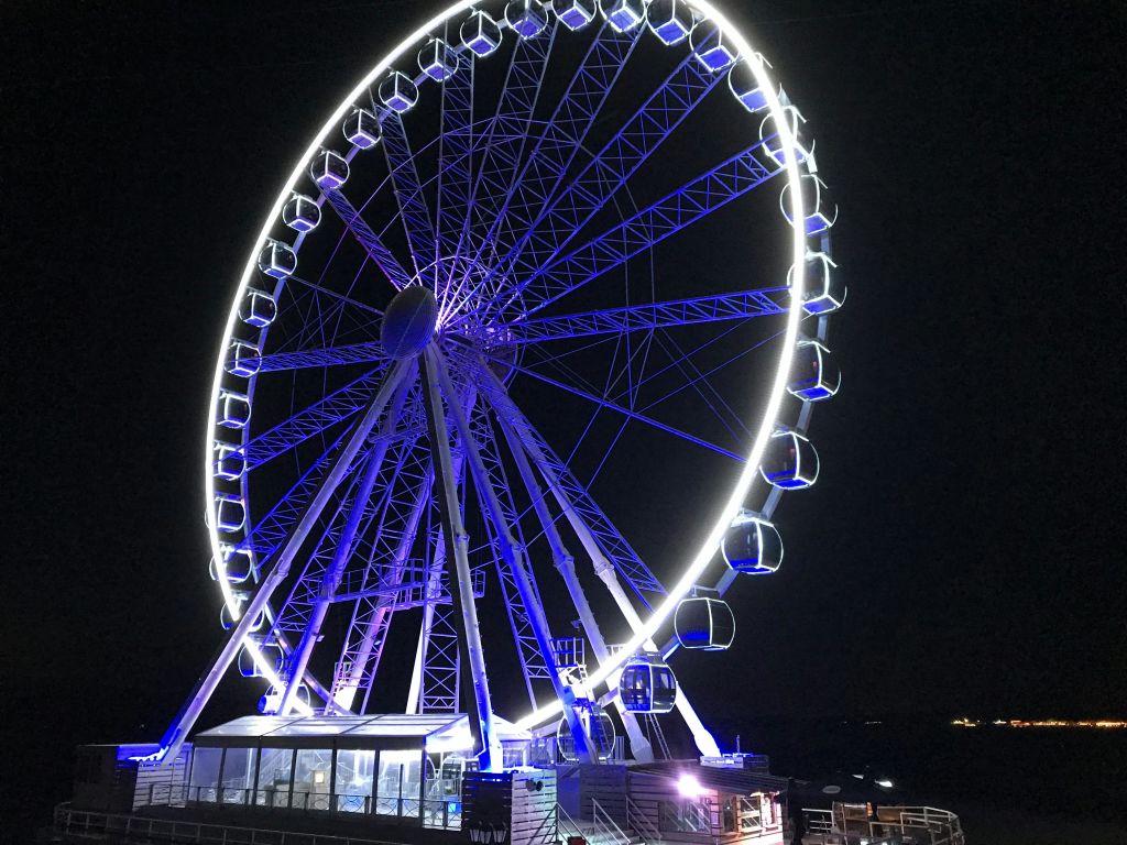 야간에는 파란색과 흰색 조명으로 조명이 켜진 동봉된 통나무집이 있는 밝은 조명 대관람차입니다.