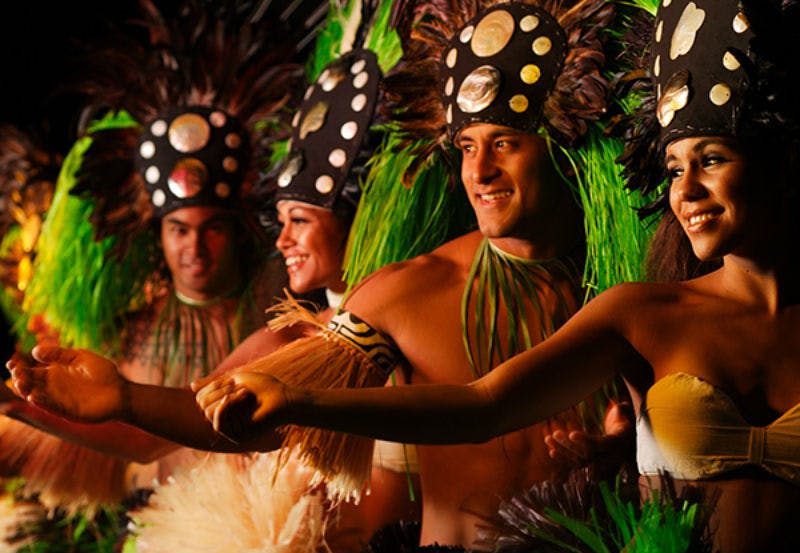 깃털 장식의 머리 장식과 팔띠가 달린 활기찬 전통 의상을 입고 춤을 추는 사람들.