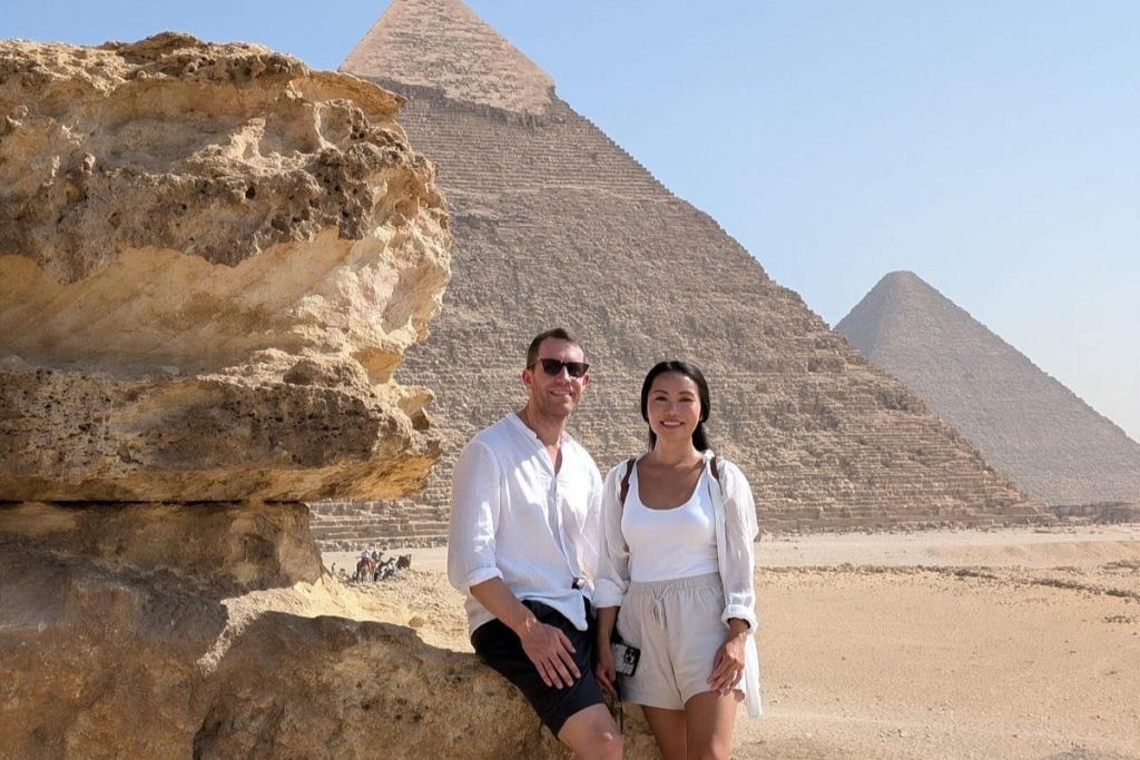 화창한 날 기자의 피라미드 앞에서 한 남녀가 커다란 바위 지층을 왼쪽에 두고 포즈를 취하고 있다.