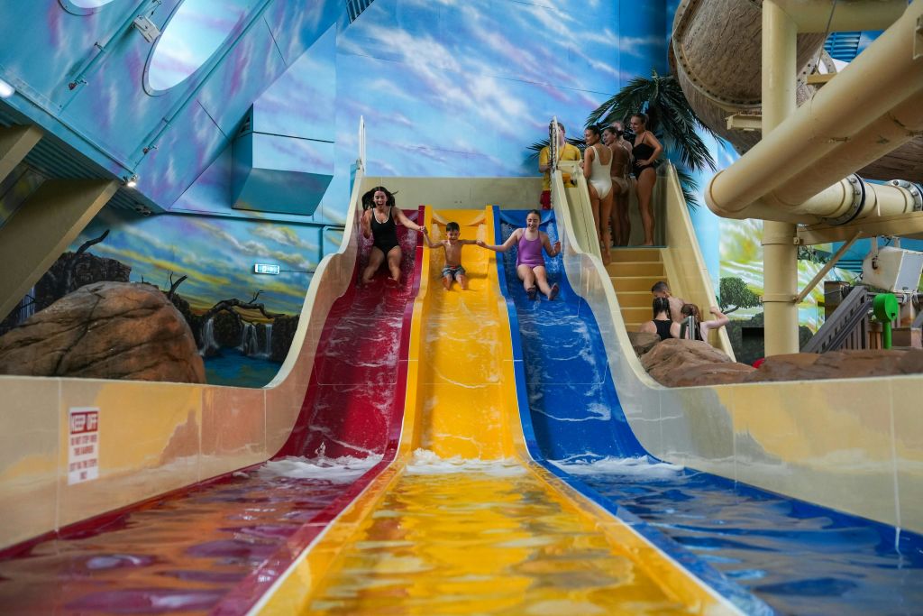 테마가 있는 실내 워터파크에서 다채로운 색상의 워터 슬라이드를 따라 미끄러져 내려오는 어린이와 어른을 위한 공간으로, 하늘을 배경으로 그림이 그려져 있습니다.