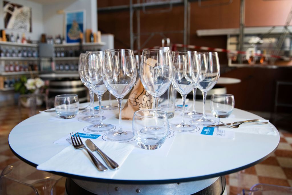 레스토랑이나 시음실에 여러 개의 와인잔, 물잔, 냅킨, 식기류, 종이봉투가 놓인 원형 테이블입니다.
