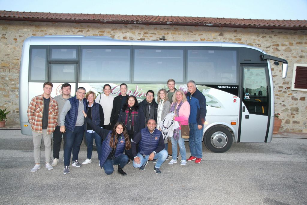 맑은 날 14명이 주차된 투어 버스 앞에서 포즈를 취하고 있습니다. 대부분 웃으며 캐주얼한 옷을 입고 있습니다.