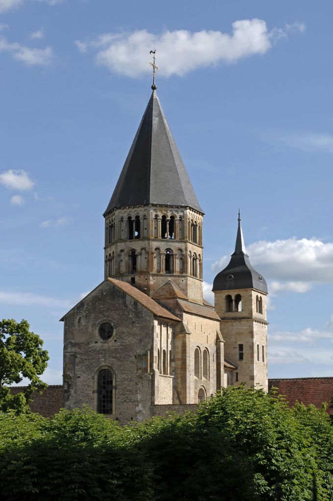 높고 뾰족한 중앙 탑과 몇 개의 구름이 있는 푸른 하늘을 배경으로 작은 둥근 종탑이 있는 석조 교회.