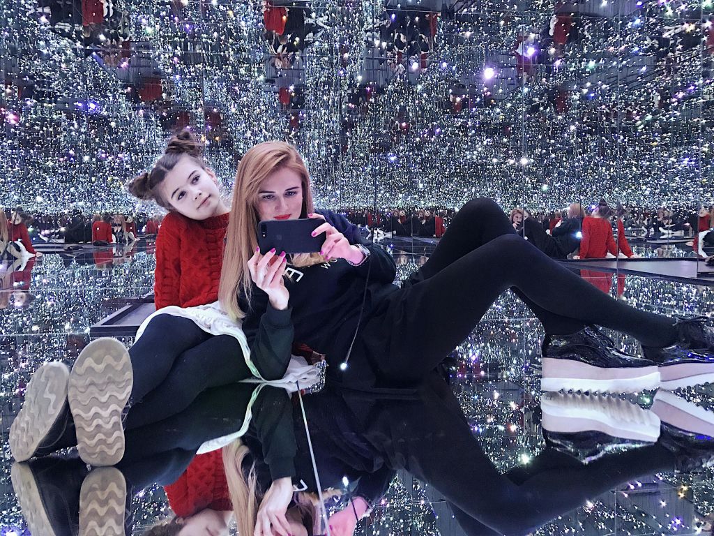 수많은 작은 불빛이 비추는 미러룸에서 포즈를 취하는 두 사람이 반짝반짝 빛나는 무한 반사 효과를 연출합니다.