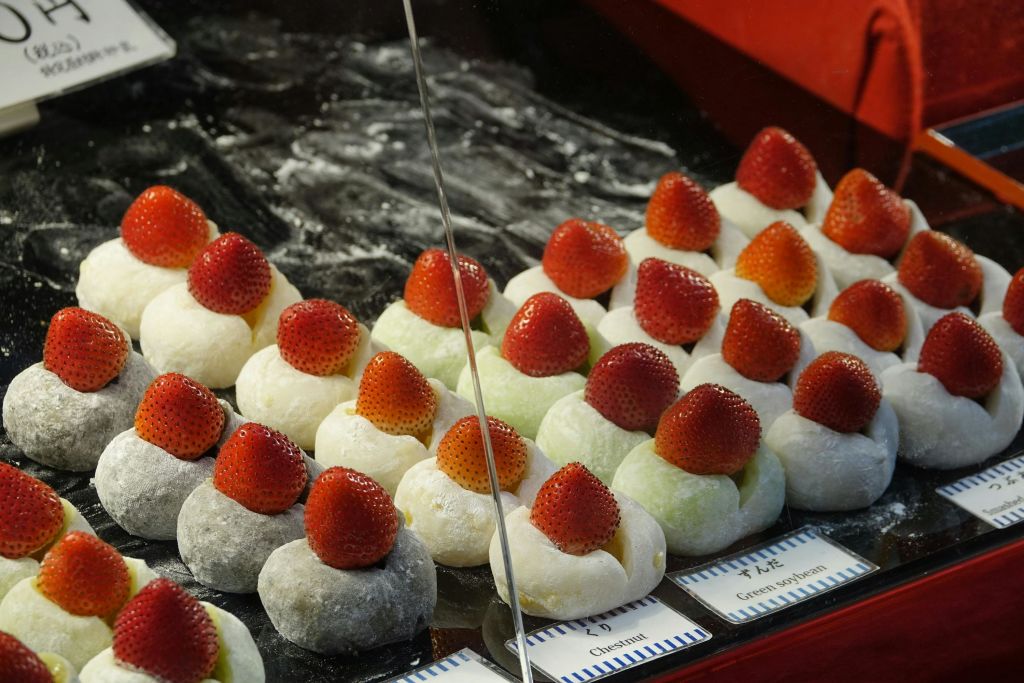 디스플레이 케이스에 딸기 전체를 얹은 모찌 볼이 줄지어 있습니다. 모찌는 흰색과 녹색 등 다양한 색상으로 제공됩니다.