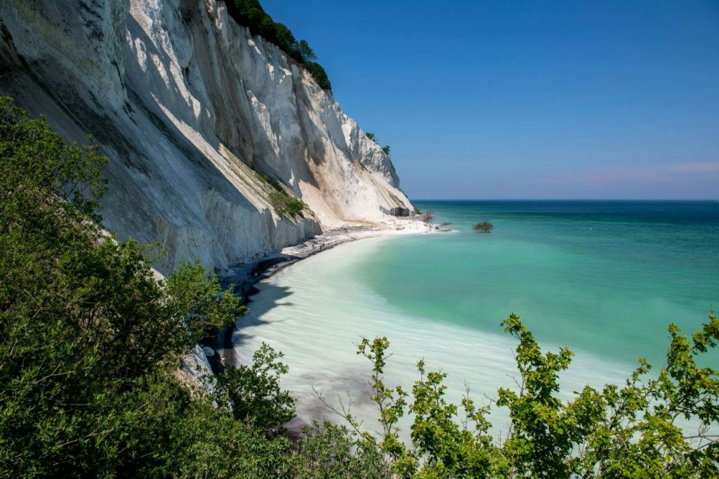 맑고 푸른 하늘 아래 하얀 절벽, 푸른 물, 초목이 어우러진 해안 풍경.