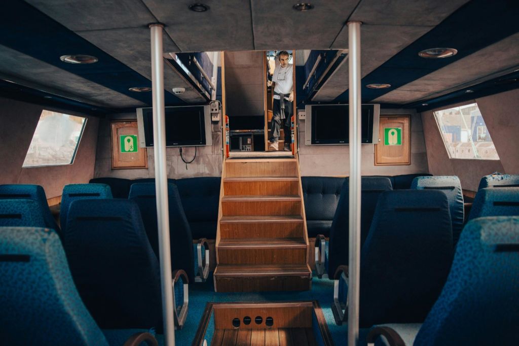 파란색 좌석이 있는 차량이나 선박의 내부, 나무 계단, 계단 꼭대기에 서 있는 사람.