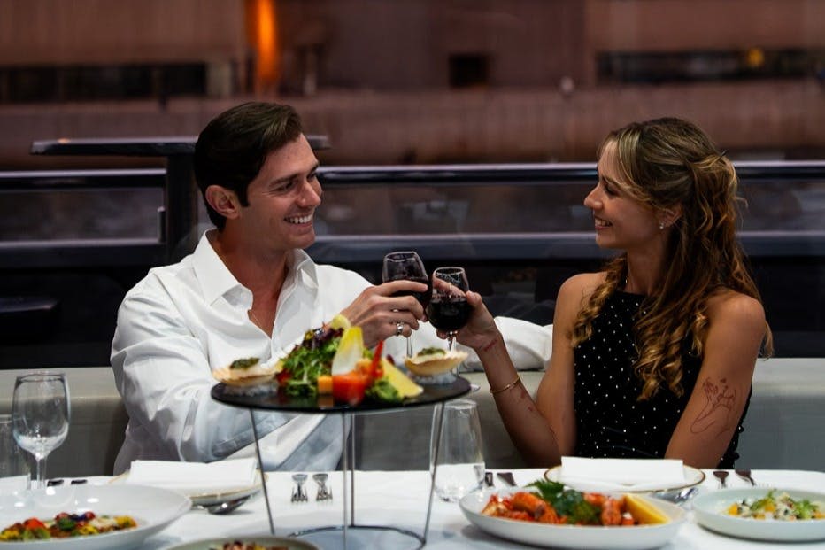 요리와 애피타이저가 있는 레스토랑 테이블에서 누군가와 하얀 셔츠를 입은 남성이 미소를 지으며 와인잔을 움켜쥐고 있습니다.