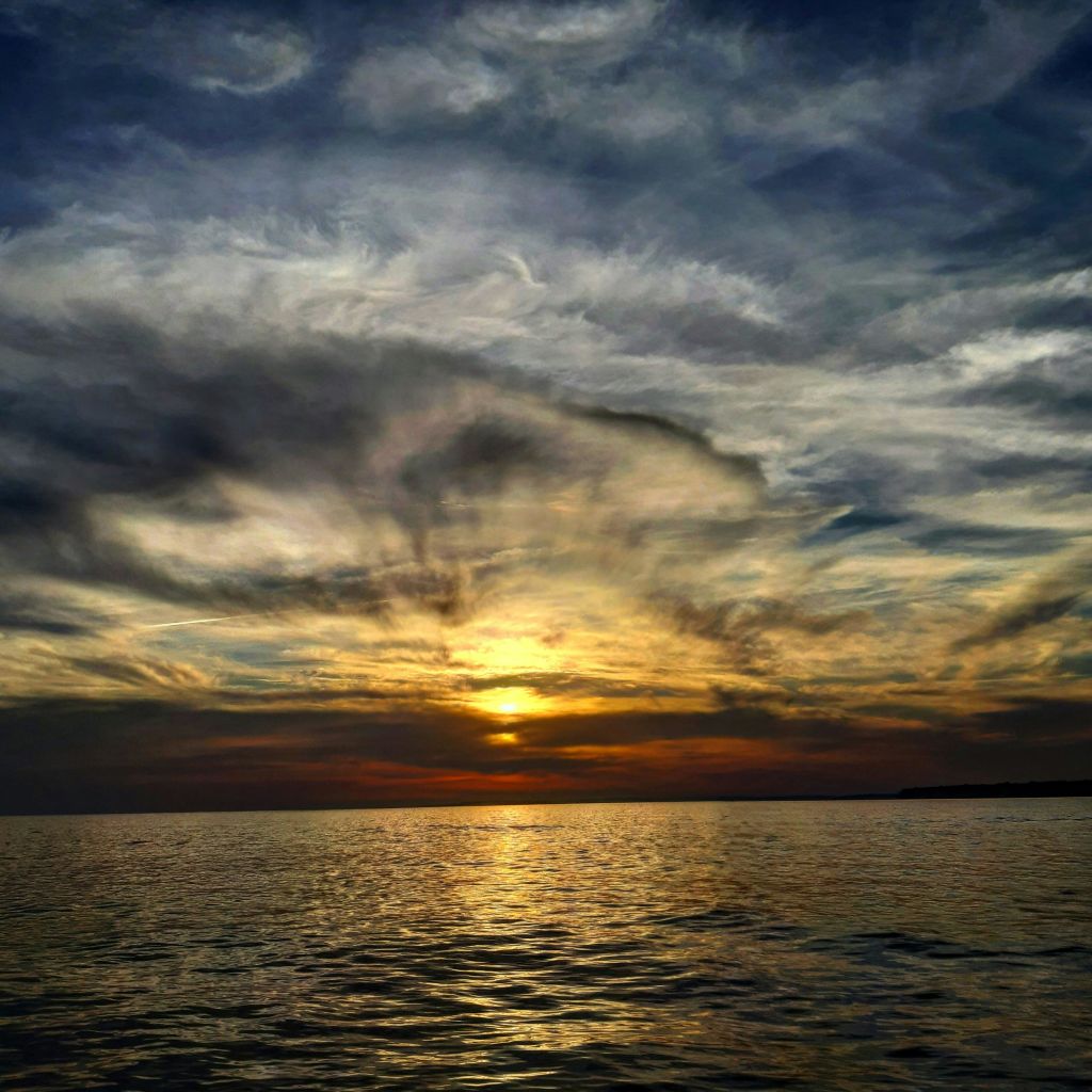 드라마틱하고 소용돌이치는 구름으로 가득한 잔잔한 바닷물 위로 지는 석양.