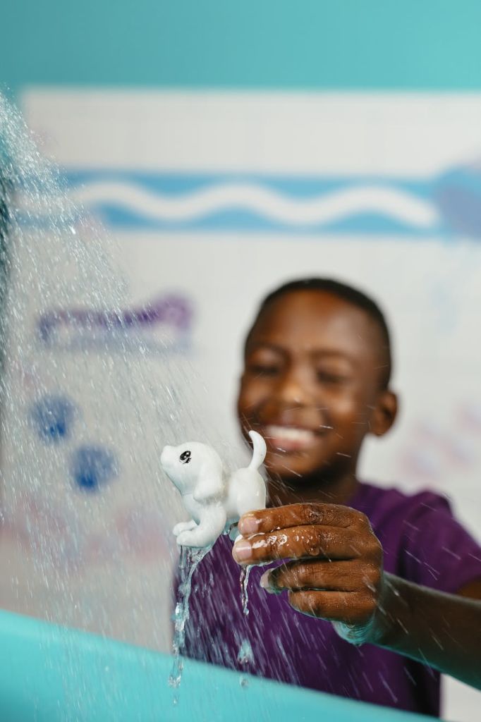 흐르는 물 아래 작은 흰색 장난감을 들고 흐릿한 배경으로 웃고 있는 아이.