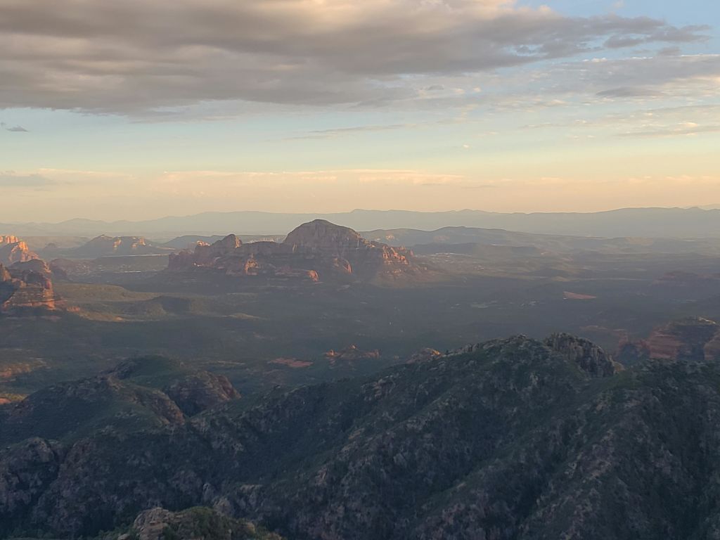 해가 지는 동안 광활한 산의 풍경을 조망할 수 있으며, 겹겹이 쌓인 산맥과 부분적으로 흐린 하늘이 특징입니다.