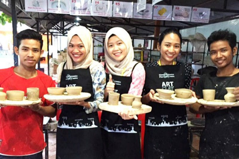 공방에서 앞치마를 두른 채 쟁반에 도자기 조각을 올려놓고 웃고 있는 네 사람.