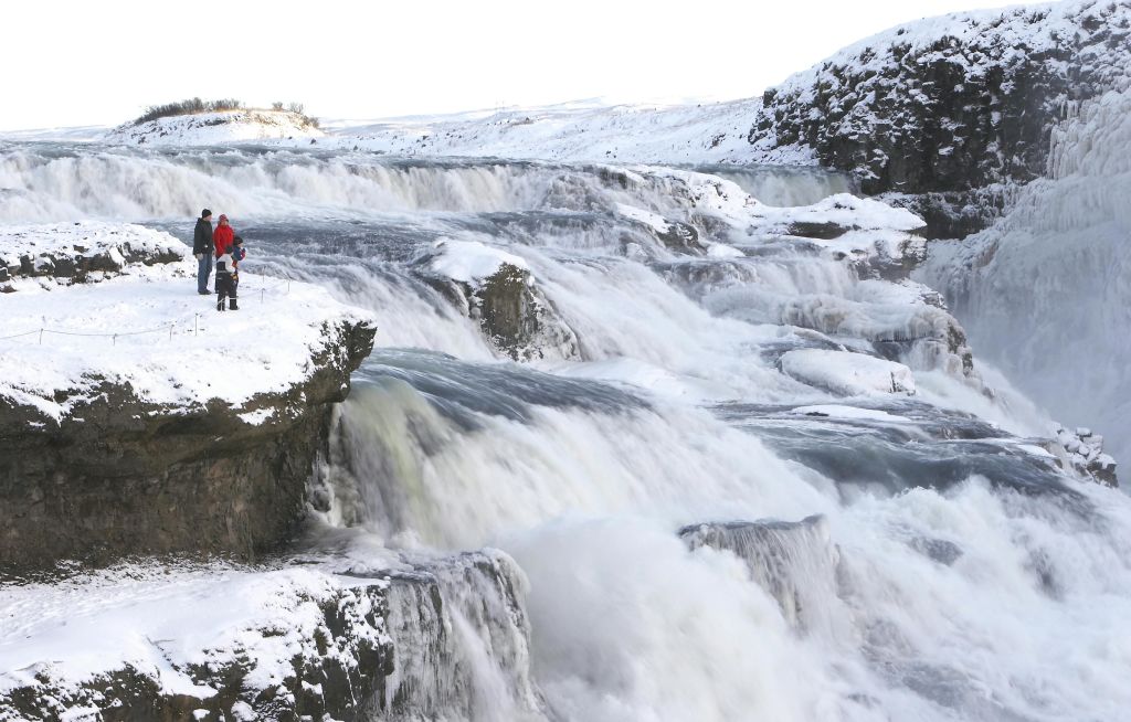 계단식 폭포와 절벽 가장자리에 서 있는 겨울 옷을 입은 두 사람이 있는 눈 덮인 풍경.