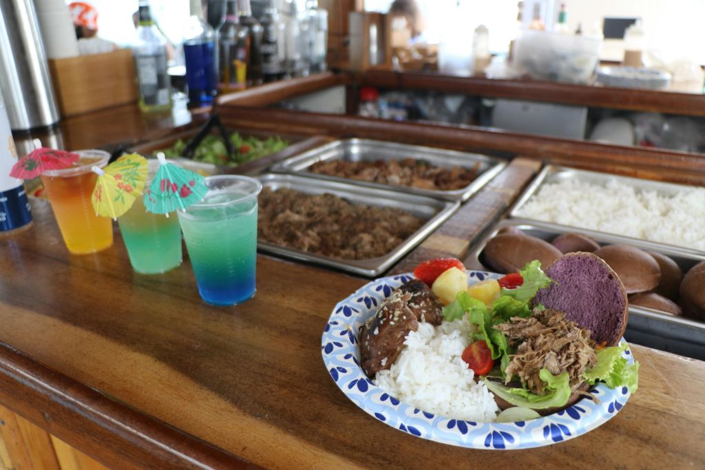 다채로운 음료 2잔과 음식 서빙 스테이션 옆에 있는 나무 카운터에 밥, 고기, 야채가 담긴 음식 접시.