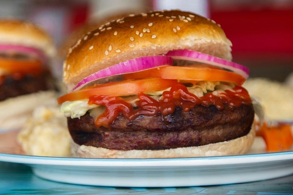 흰 접시에 양파, 토마토, 양상추, 케첩을 얹은 참깨빵을 곁들인 햄버거 클로즈업.