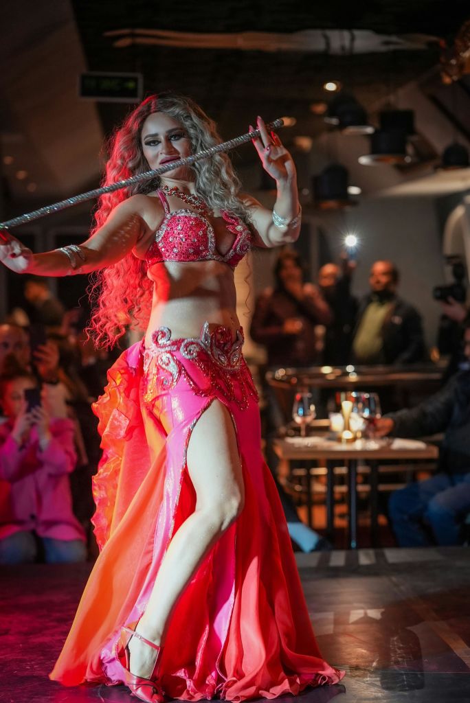 밝은 분홍색 의상을 입은 여성이 조명이 희미한 레스토랑에서 검을 들고 춤을 추고 있습니다.