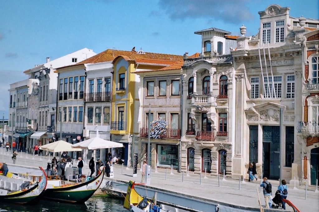 다채롭고 화려한 건물이 운하를 따라 배가 정박해 있습니다. 보행자들은 맑은 하늘 아래 물가를 따라 걷습니다.