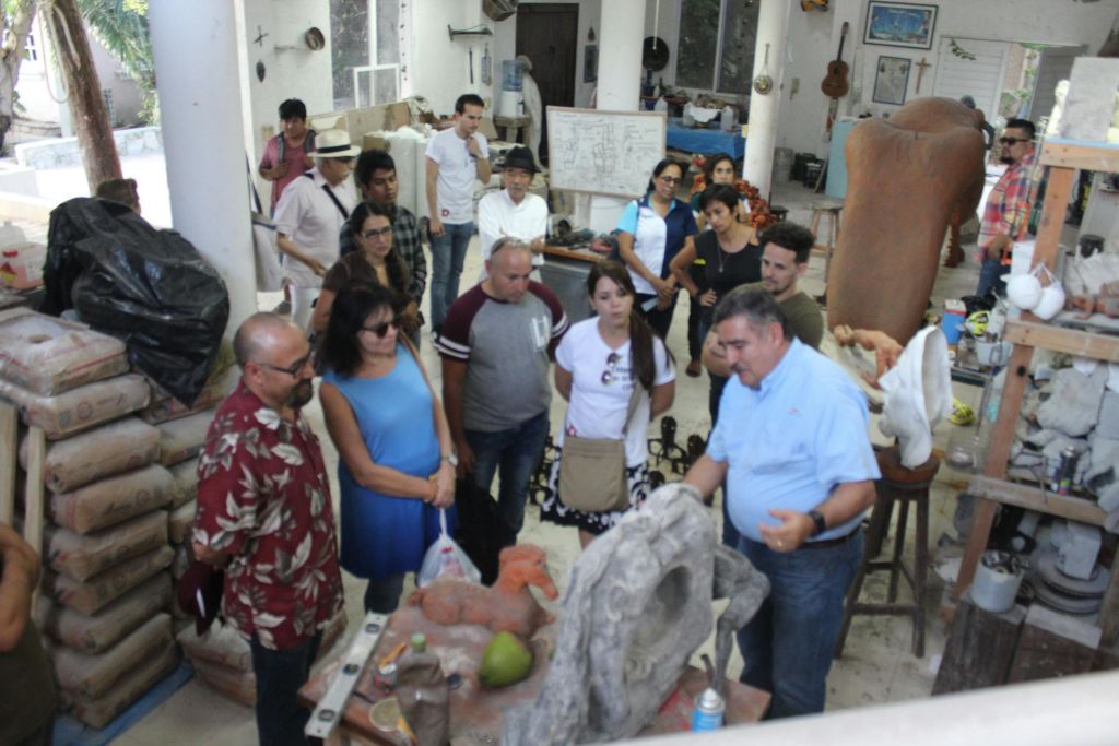 작업실에 있는 한 무리의 사람들이 도구, 조각품, 무언가를 시연하는 사람이 있는 테이블에 모여듭니다.