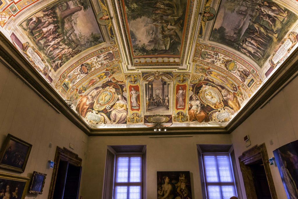 정교한 프레스코화와 빛이 들어오는 두 개의 창문이 있는 페인트 천장이 있는 풍부하게 꾸며진 객실입니다.