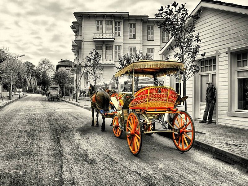 밝은 노란색 바퀴가 달린 마차와 오래된 건물과 나무가 늘어선 거리에 주황색 좌석이 있습니다.