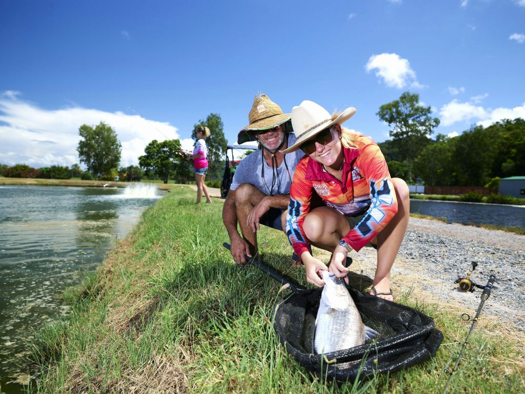 화창한 날 연못가에서 커다란 물고기를 잡고 있는 밀짚모자를 쓴 두 사람이 근처에 바닥에 낚시 장비를 갖추고 있습니다.