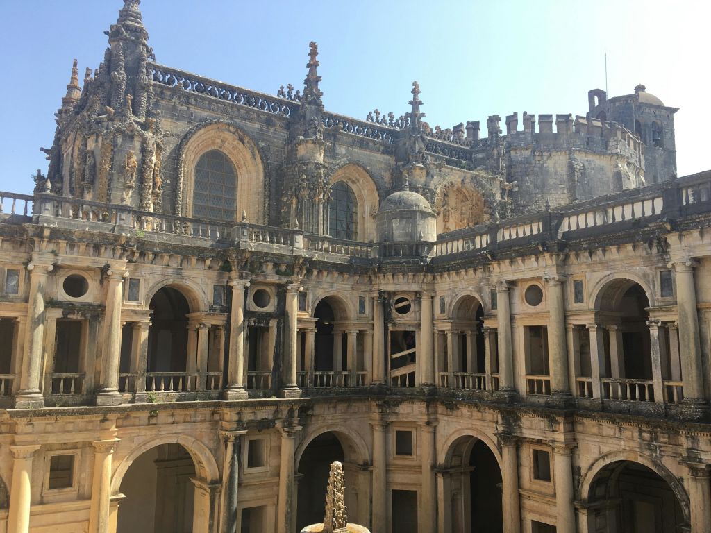 맑고 푸른 하늘 아래, 여러 개의 아치, 디테일한 돌 조각, 커다란 아치형 창문이 있는 화려한 고대 건물.
