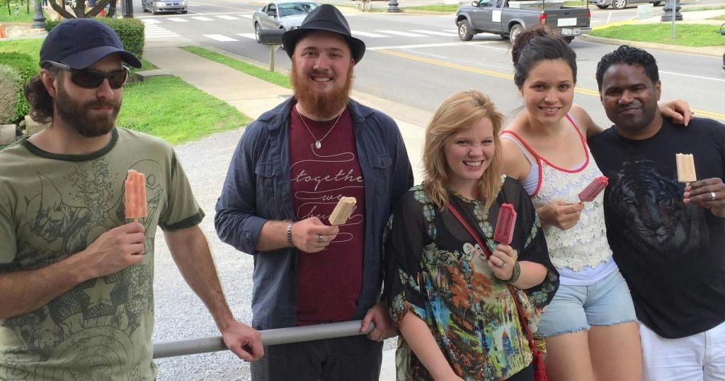 주차된 차와 잔디를 배경으로 거리 근처 야외에서 아이스하키를 보며 웃고 있는 네 사람.