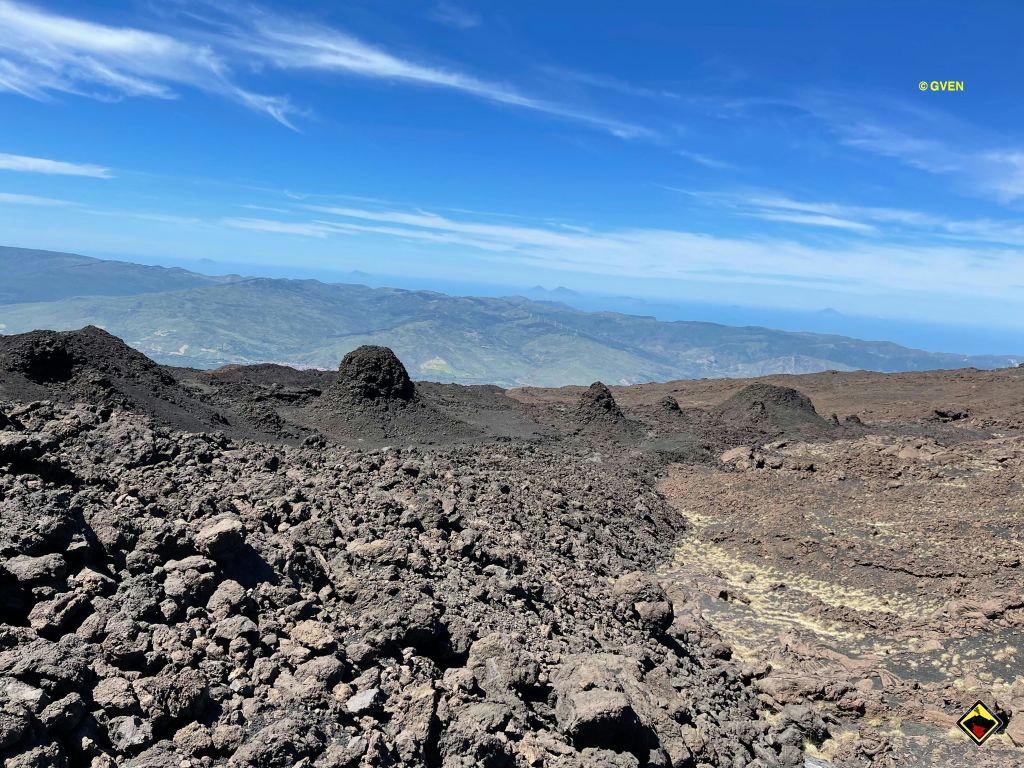 맑고 푸른 하늘 아래 어두운 들쭉날쭉한 바위가 있는 바위 화산 풍경. 배경으로 보이는 산과 계곡.