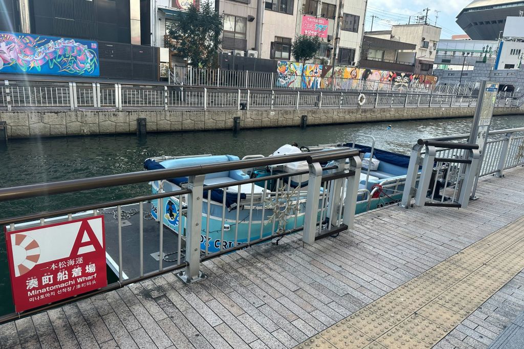 운하 옆에 정박한 작은 보트로, 전경에 금속 난간과 벽돌 통로가 있고, 건물을 배경으로 한 건물이 있습니다.