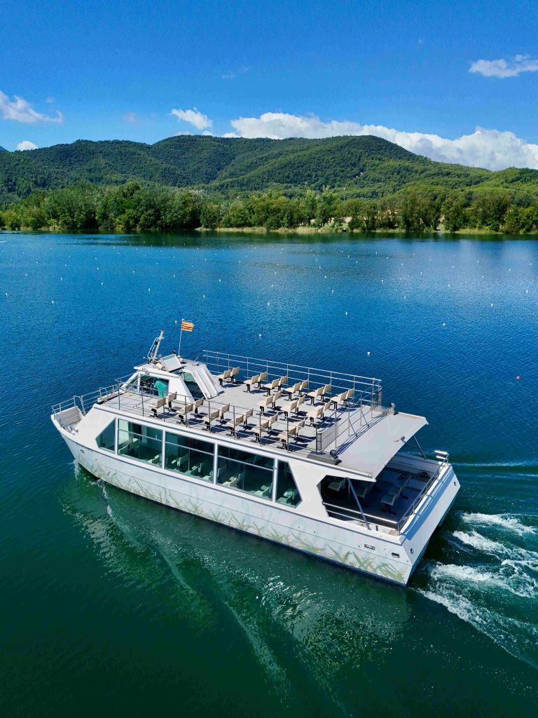 숲이 우거진 언덕과 부분적으로 흐린 하늘을 배경으로 맑은 호수에서 크루즈를 즐기는 현대적인 보트.