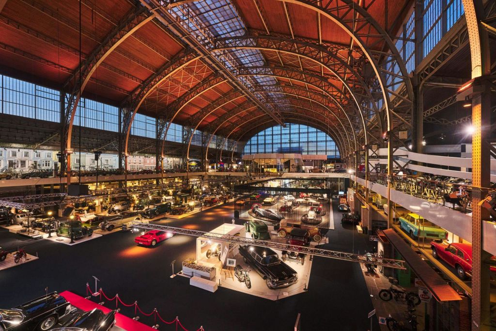 수많은 빈티지 차량, 조명 디스플레이, 아치형 나무 천장이 있는 넓은 자동차 박물관 홀.