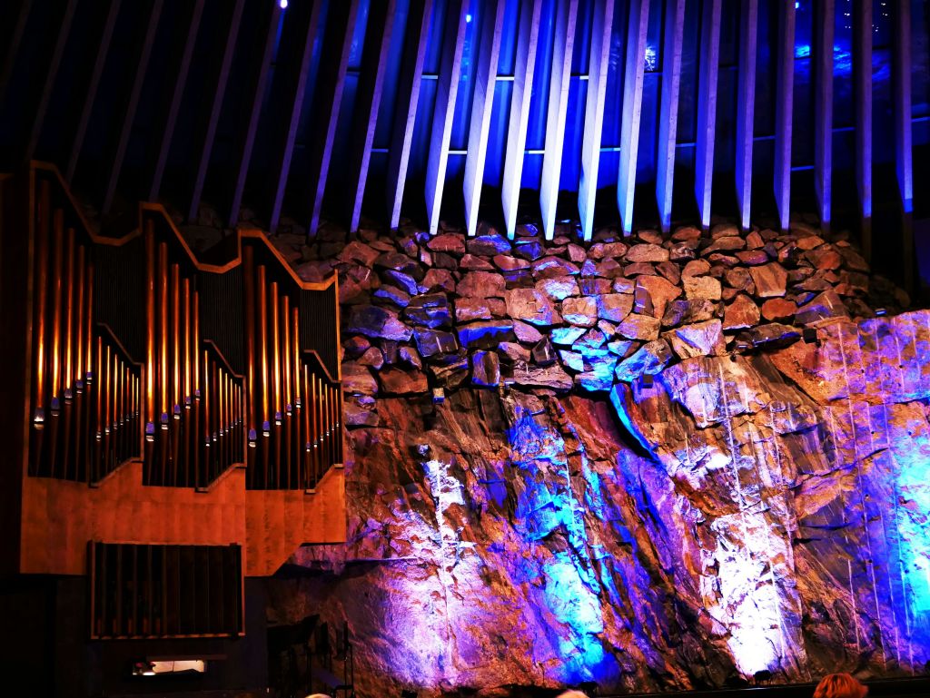 커다란 파이프 오르간과 뾰족한 천장 기둥 옆에 파란색과 보라색 조명이 있는 암벽.