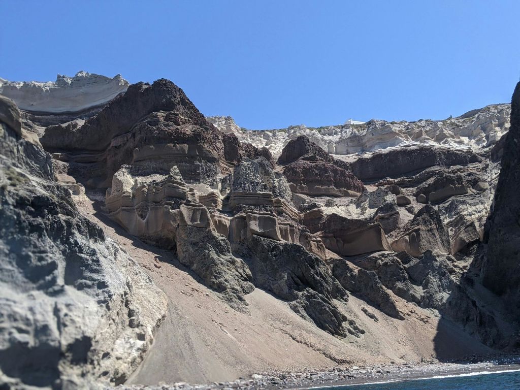 맑고 푸른 하늘 아래 갈색과 베이지 색으로 겹겹이 쌓인 절벽, 바닥에 바위 지형이 있습니다.