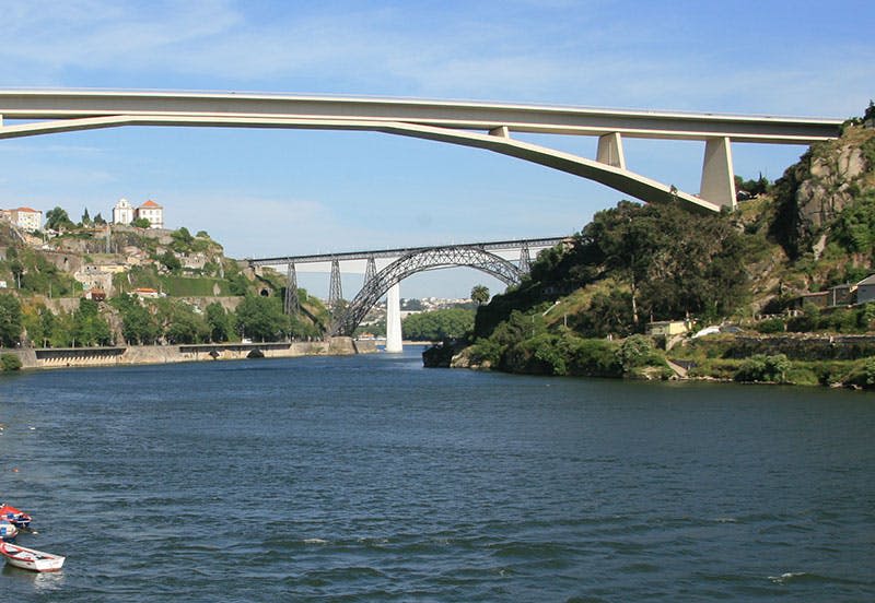 맑고 푸른 하늘 아래 푸른 언덕과 절벽 옆 건물이 있는 강변에는 두 개의 다리가 놓여 있습니다.