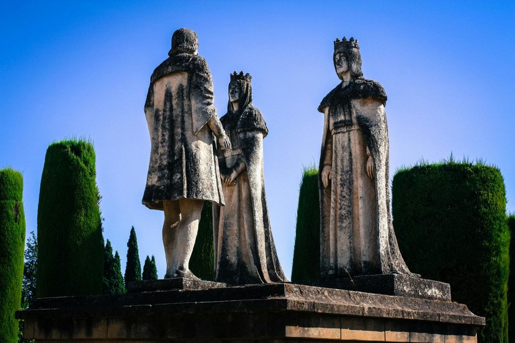 왕관과 망토를 두른 석상 세 개가 플랫폼에 서 있으며, 높고 푸른 하늘에 둘러싸여 있습니다.