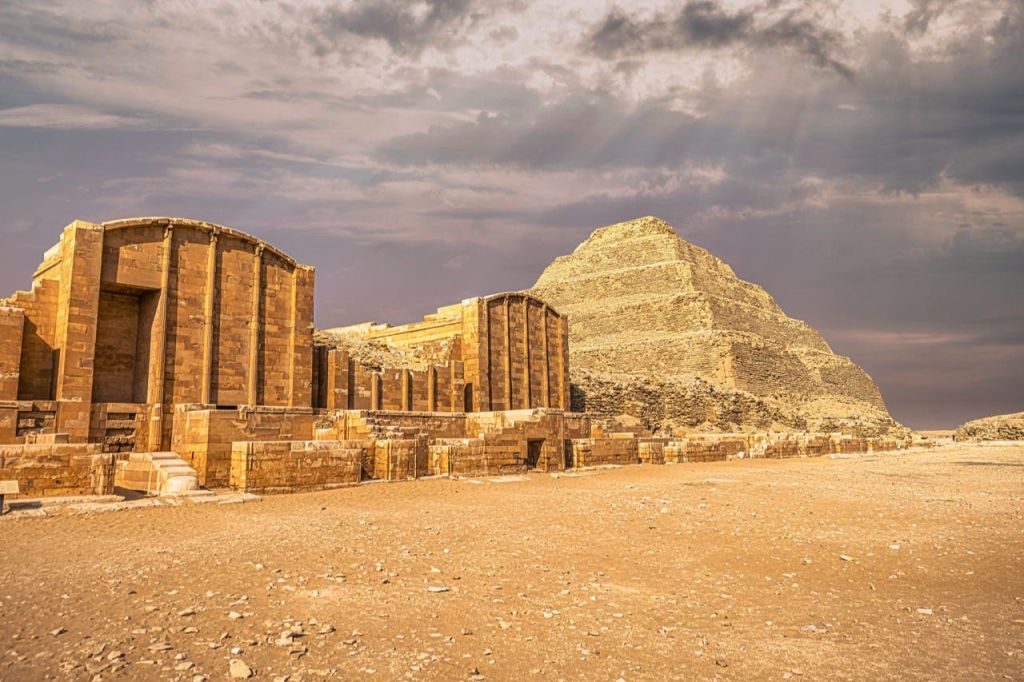 Djoser의 계단 피라미드와 이집트의 고대 석조 구조물, 햇살이 내리쬐는 부분적으로 흐린 하늘 아래.
