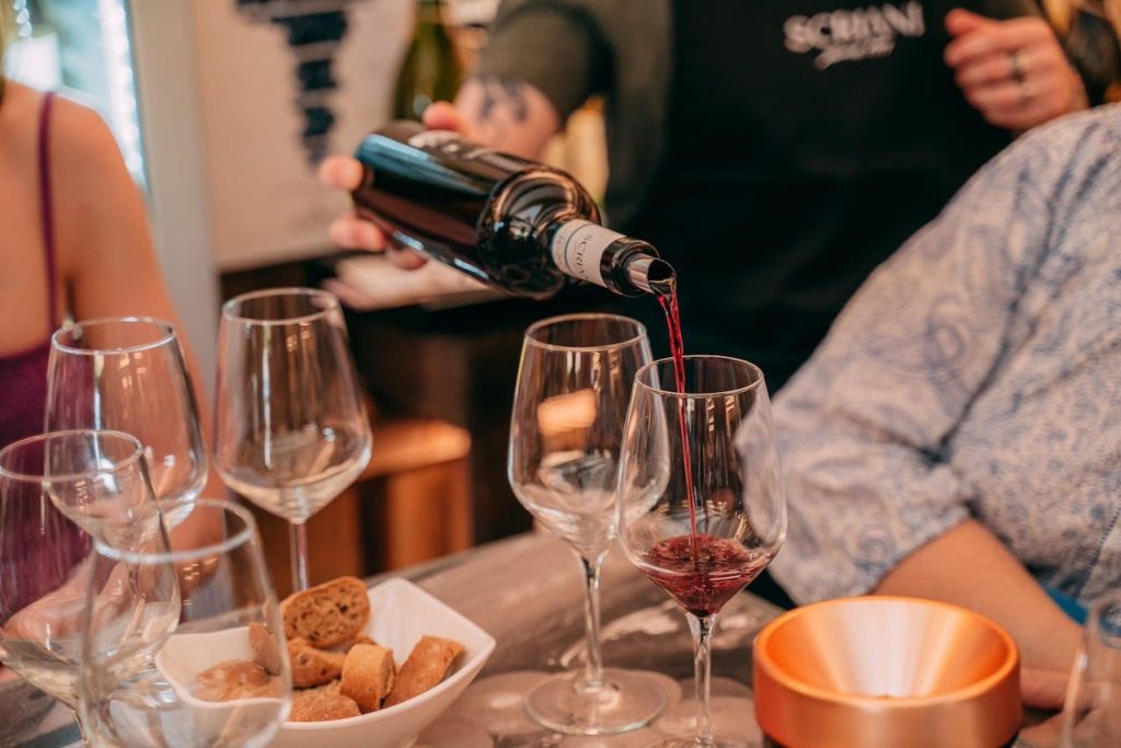 한 사람이 빵과 잔이 놓인 테이블 위에 놓인 유리잔에 레드 와인을 붓고 편안한 식사 분위기를 조성합니다.