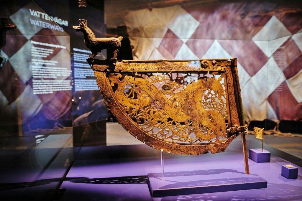 정보 패널을 배경으로 박물관에 전시된 정교한 조각이 돋보이는 화려한 목조 유물입니다.