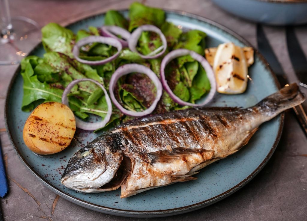 잎이 무성한 채소와 붉은 양파 링을 곁들인 사이드 샐러드와 구운 레몬 웨지를 곁들인 접시에 구운 생선.