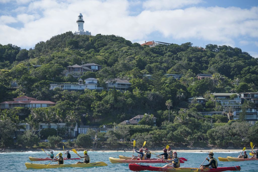 숲이 우거진 언덕과 등대를 배경으로 해변 근처에서 노를 저어보세요.