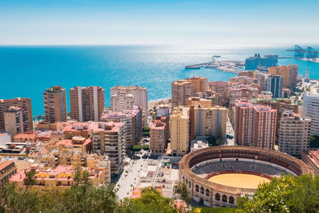 고층 건물, 원형 황소 고리, 맑은 하늘 아래 잔잔한 푸른 바다로 뻗은 항구가 있는 해안 도시의 전망.