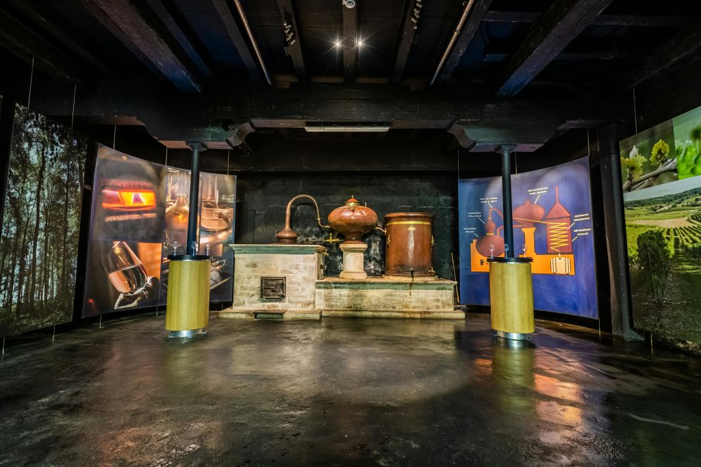 조명이 희미한 방에 정보 패널로 둘러싸인 구리 증류 장비를 전시하는 전시품.