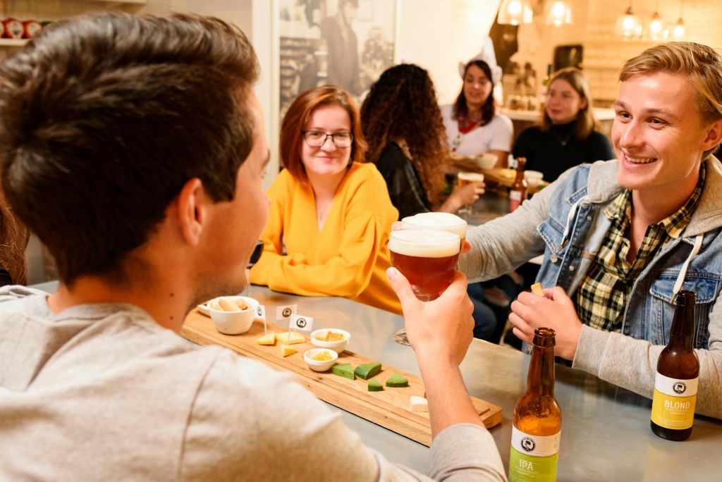 바에서 맥주와 함께 건배하는 사람들; 테이블 위에 놓인 다양한 작은 요리들. 백그라운드에서 미소를 짓는 후원자.