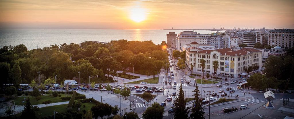 바다를 배경으로 나무가 우거진 공원, 건물, 번화가, 차량이 있는 해안 도시의 석양 풍경.