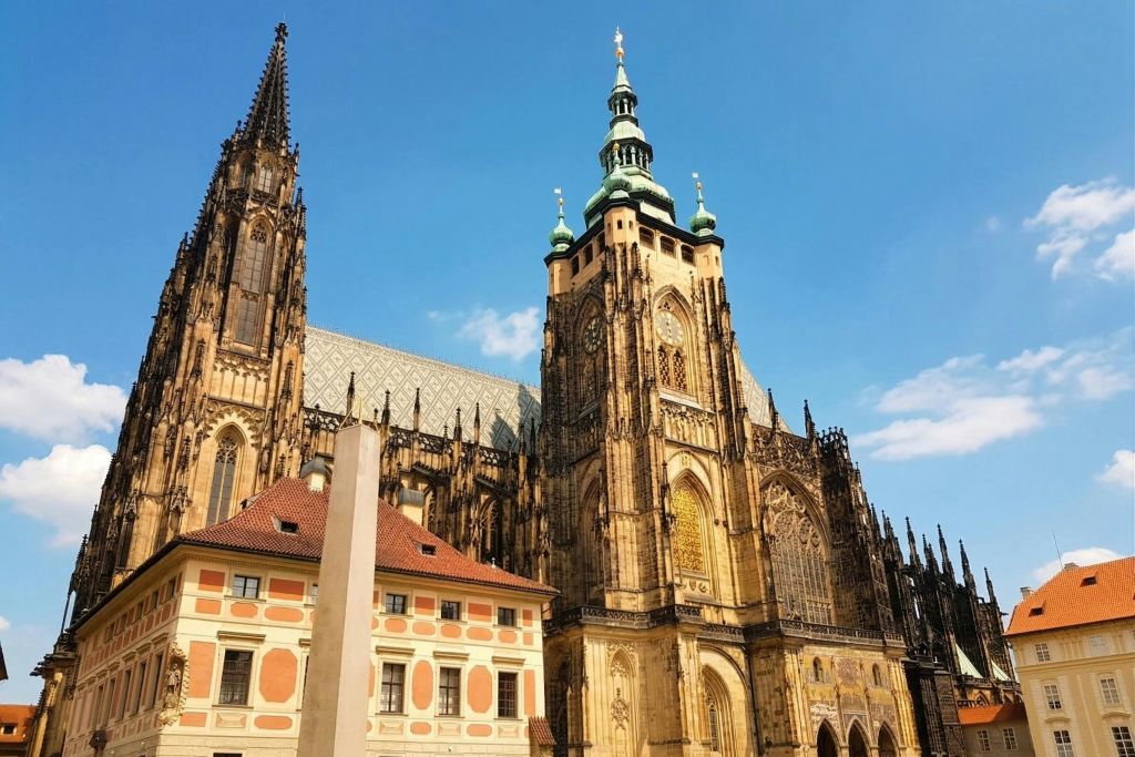 맑고 푸른 하늘 아래 화려한 건물 옆에 정교한 첨탑과 탑이 있는 고딕 양식의 대성당입니다.