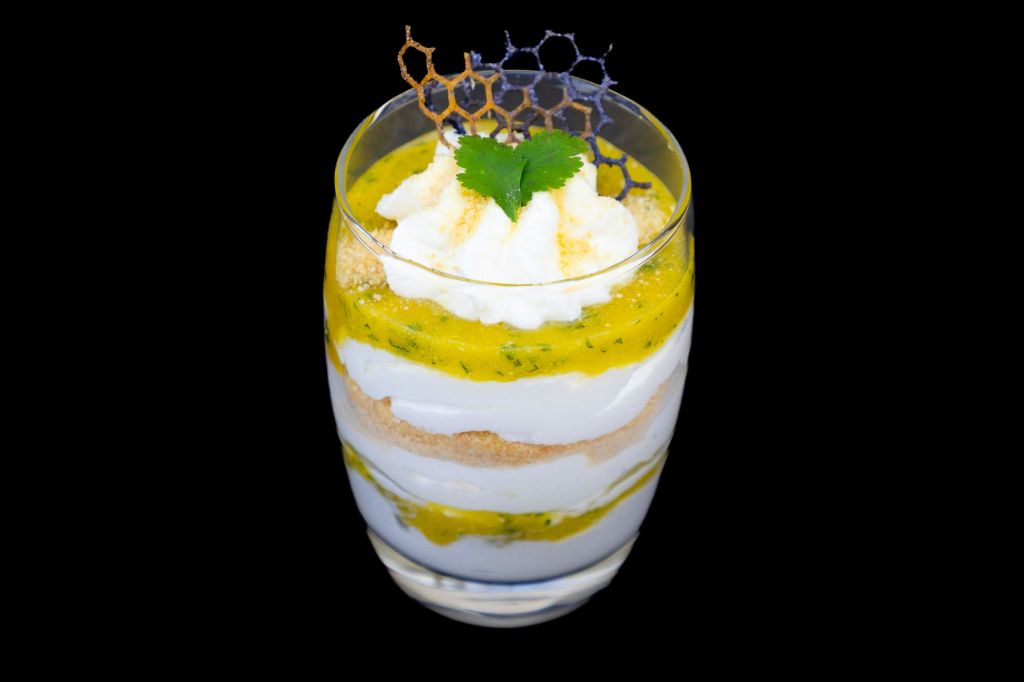 그 위에 휘핑 크림, 옐로우 소스, 크럼블, 장식용 벌집 장식이 들어간 컵에 담긴 레이어드 디저트입니다.