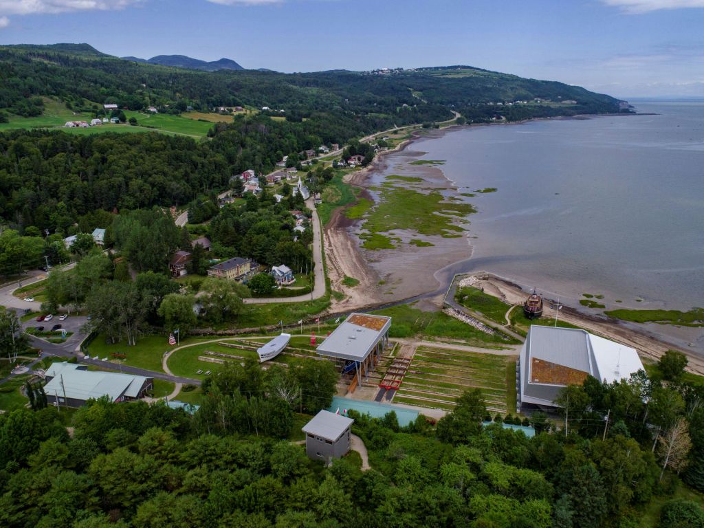 건물, 녹색 언덕, 물가에 진흙 투성이의 해안선이 있는 해안 마을의 공중 전망.