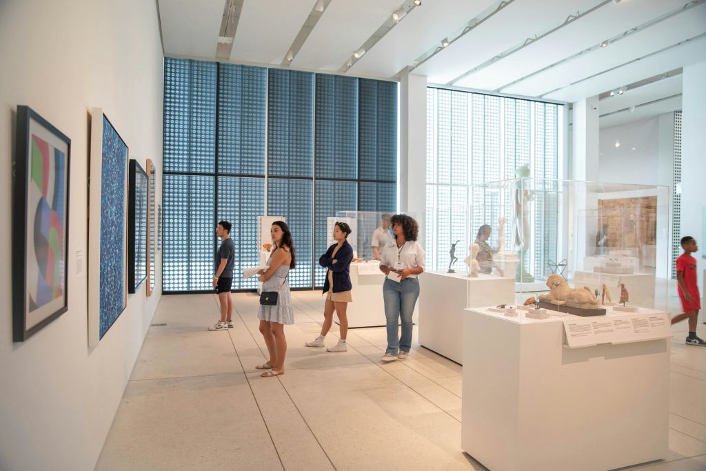 커다란 창문과 밝은 조명이 있는 현대 미술관에서 예술 작품을 감상하는 사람들.